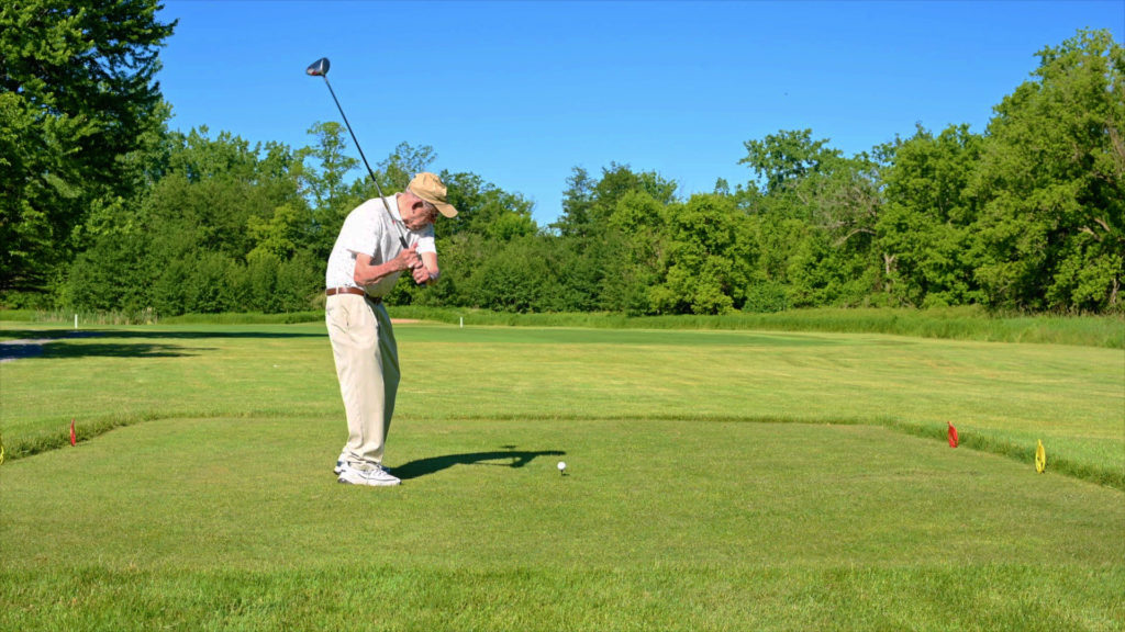 A senior golfer drives from the tee of a secluded course on a gorgeous sunny day