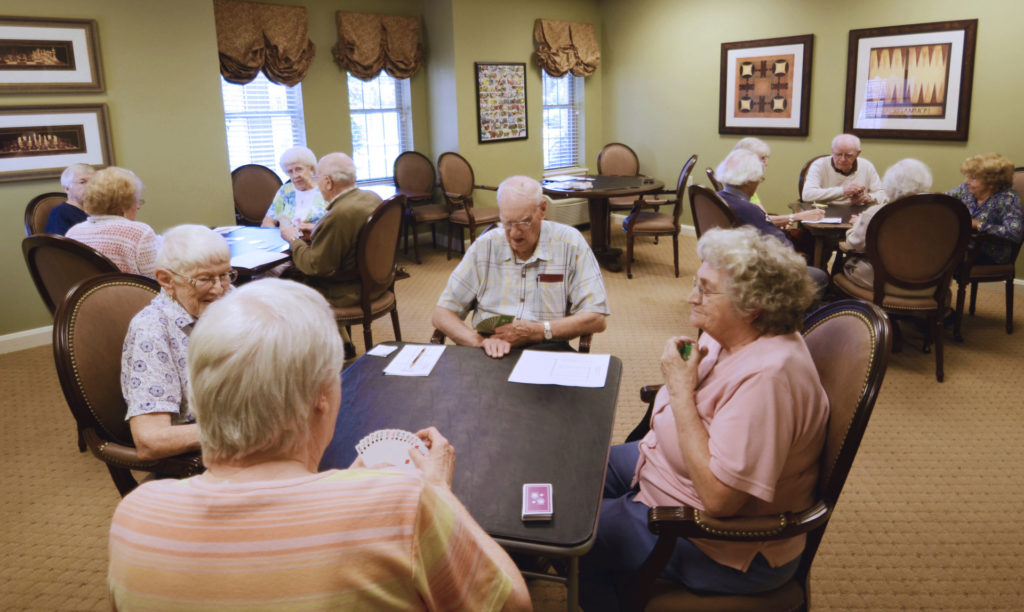 The game room hosts a Bridge tournament with several tables of card players all playing to win.